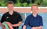 2 Jungen, die Pool-Nudeln tragen, im Hintergrund ein Schwimmbad