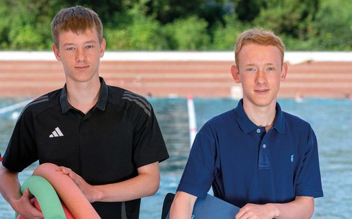 2 Jungen, die Pool-Nudeln tragen, im Hintergrund ein Schwimmbad