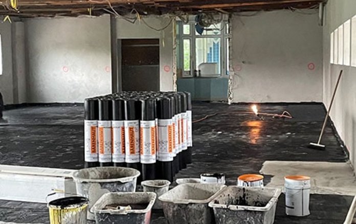 Blick in einen Raum, in dem schwarze Farbe auf den Boden aufgetragen wird zur Abdichtung