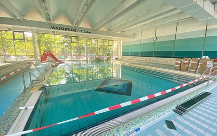Blick auf das Nichtschwimmerbecken mit roter Wasserrutsche. Davor ist ein Absperrband