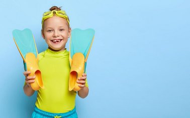 Kind mit Taucherbrille auf dem Kopf und Schwimmflossen in beiden Händen